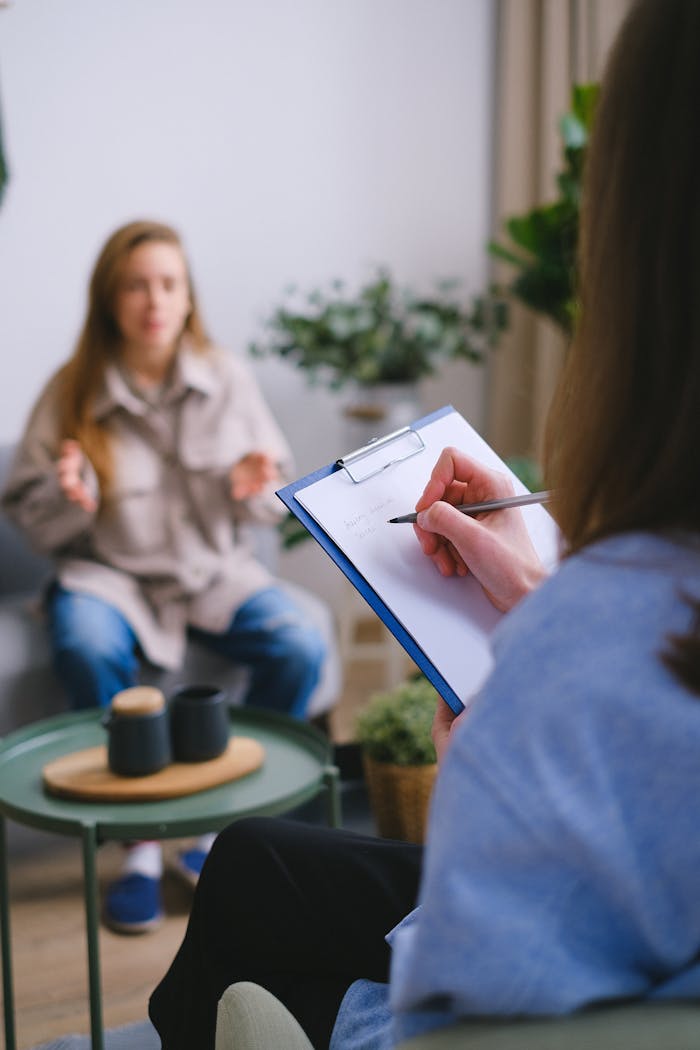 about-04 Unrecognizable female psychologist taking notes on clipboard while listening to patient sitting on blurred background during psychotherapy consultation in office