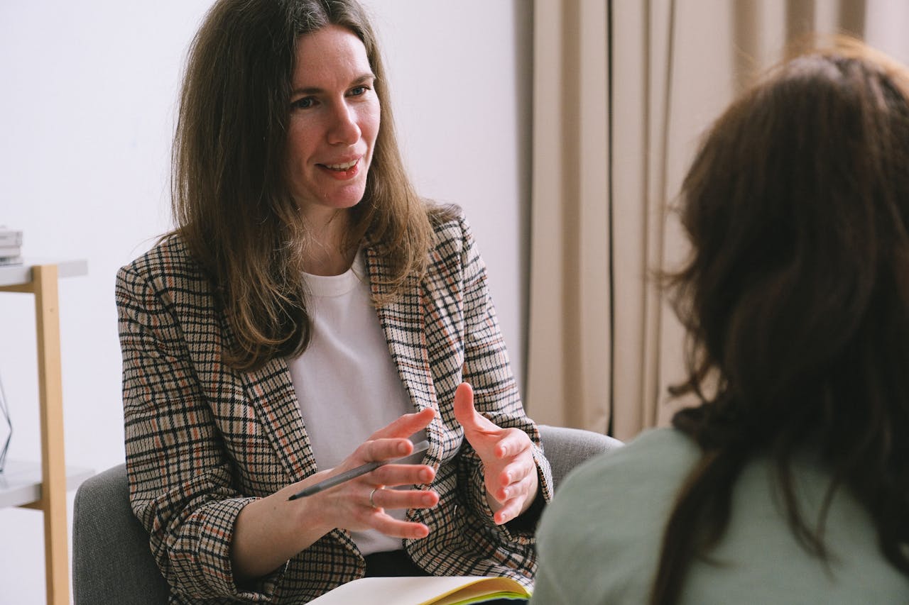 services-01 Pensive woman psychologist with brown hair in stylish clothes sitting and talking with unrecognizable female in light room